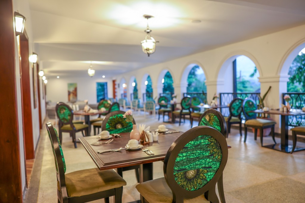 The dining room seen down its length, tables laid and cane chairs set along a run of arched windows.