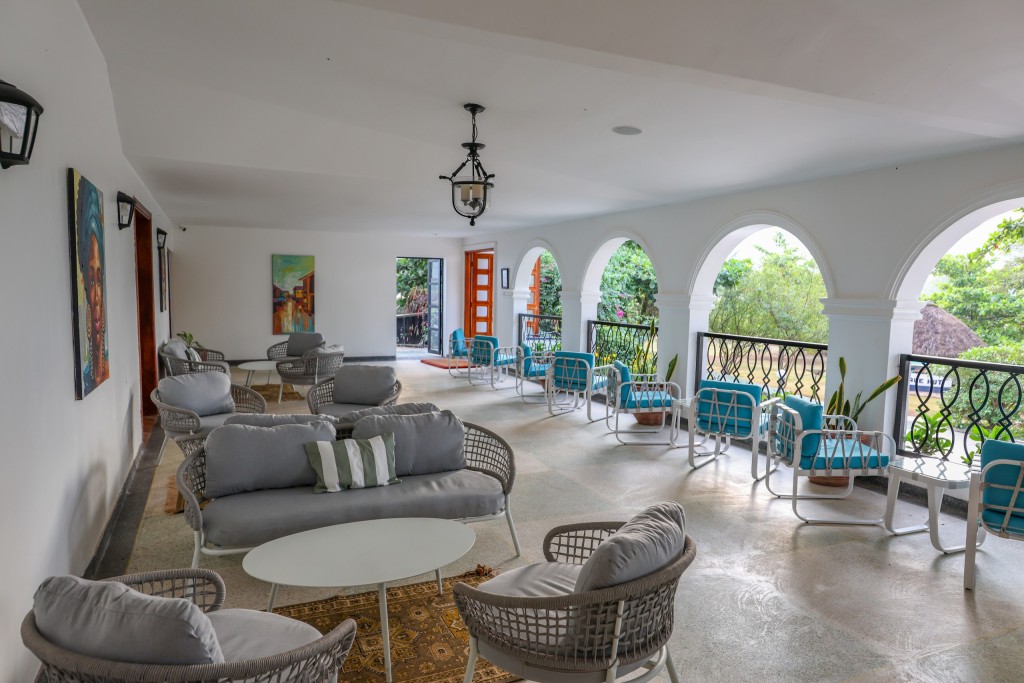 Lounge seating and low tables in the long dining room, arched windows open to the garden along one side.
