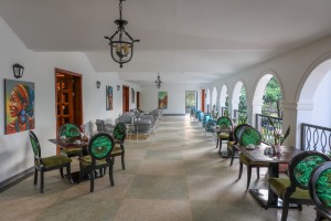 Masaaba Restaurant: tables and cane chairs along the arched veranda, hills and greenery through the openings.