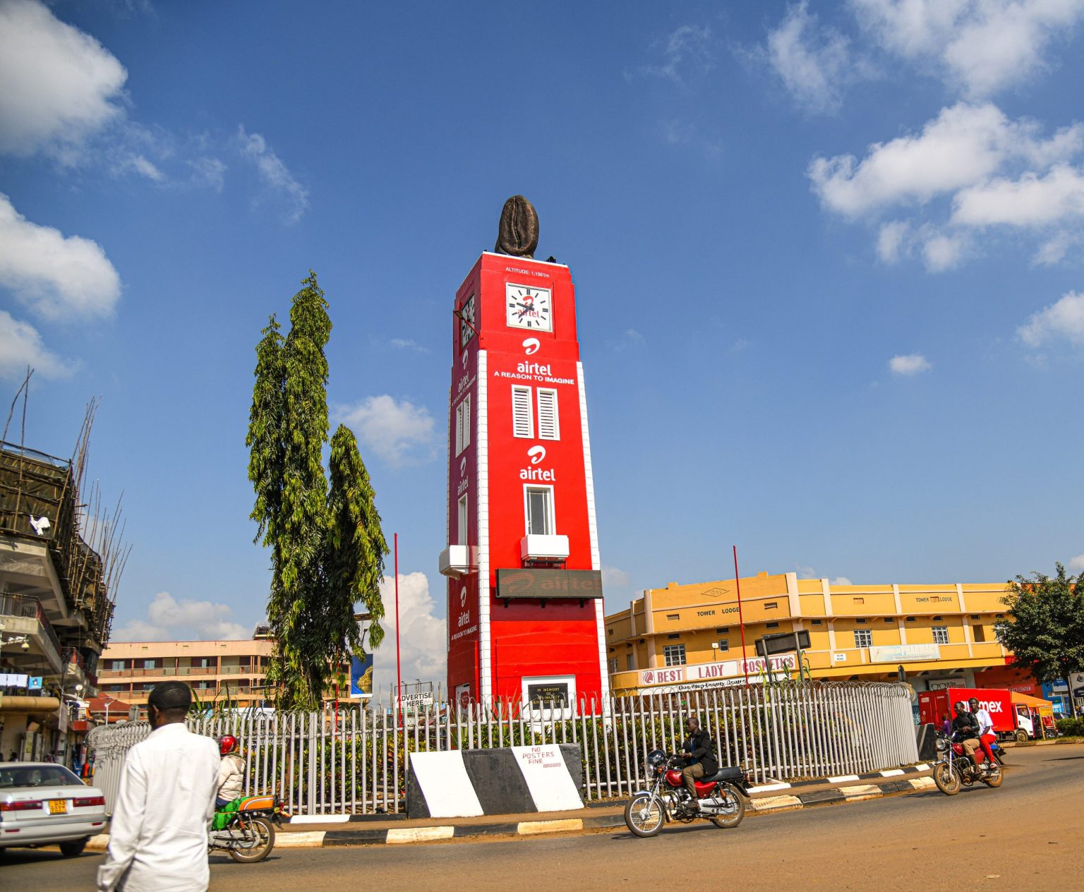 The red clock tower at the centre of Mbale town, with shops and motorcycles on the surrounding street.