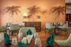 The dining room with its painted palm mural, teal napkins and carved timber furniture.