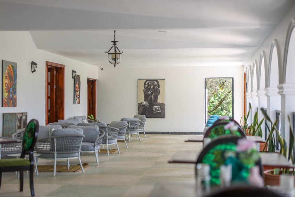 A long white room off the arcade with loose armchairs set out in groups, framed pictures along the walls.