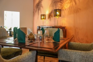 The dining room with its painted palm mural, teal napkins and carved timber furniture.
