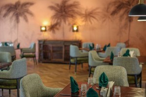 The dining room with its painted palm mural, teal napkins and carved timber furniture.