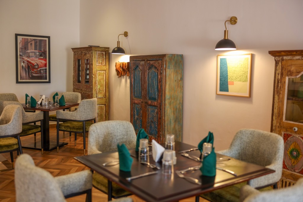 A corner table set for four beside a carved cabinet, framed pictures on the wall behind it.