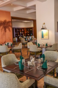 The dining room with its painted palm mural, teal napkins and carved timber furniture.