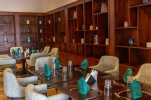 A wood-panelled dining room with upholstered chairs and tables laid for service.