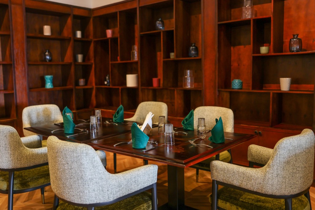 A table set for six with teal napkins in a timber-shelved room, low armchairs pulled up to it.