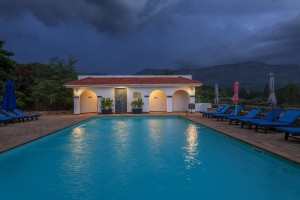 The lit pool and pavilion at dusk, with garden furniture on the terrace.