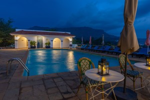 The lit pool and pavilion at dusk, with garden furniture on the terrace.