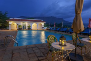 The lit pool and pavilion at dusk, with garden furniture on the terrace.