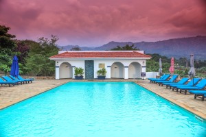 The outdoor pool and its arched pavilion under a sunset sky, blue loungers along the terrace.