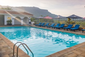 The swimming pool and its paved terrace with loungers and parasols, hills beyond.