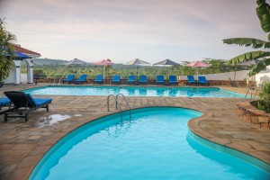 The swimming pool and its paved terrace with loungers and parasols, hills beyond.