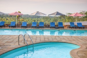 A shallow curved childrens pool in the foreground beside the main swimming pool, with open parasols shading a row of blue loungers.