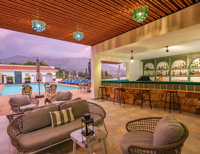 The open-sided poolside bar under its timber ceiling, cane seating in front and the pool and hills beyond.