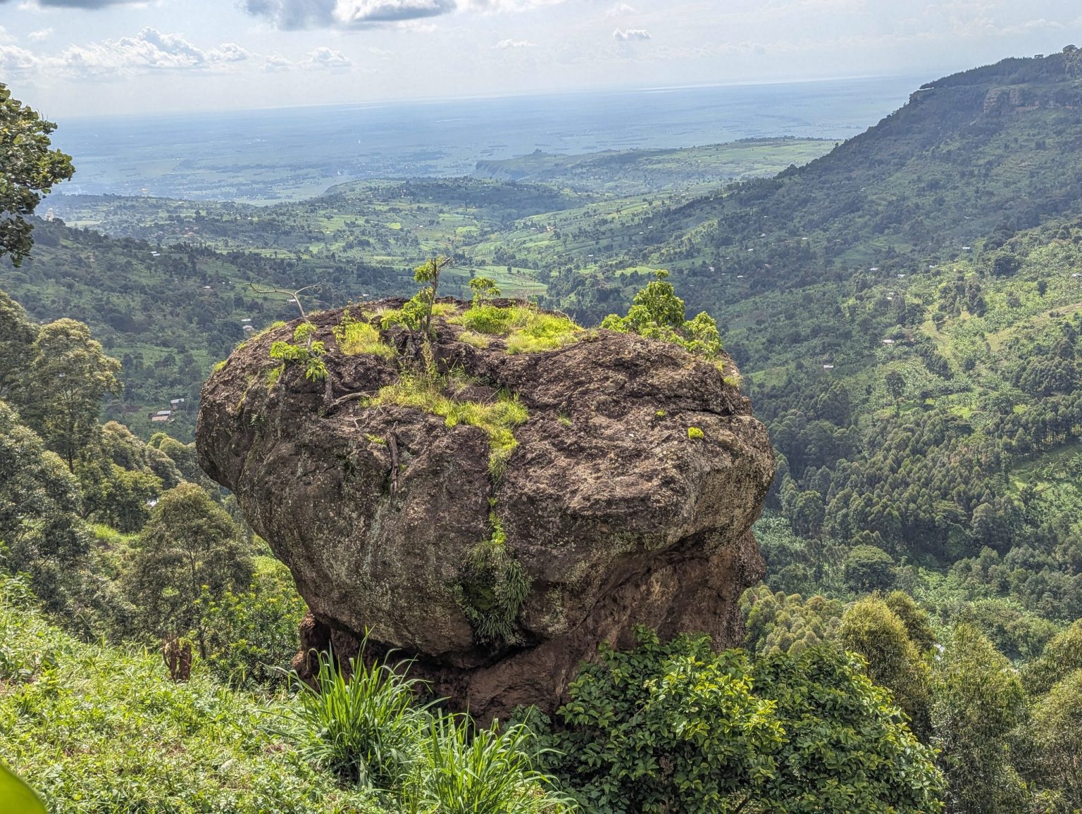 A large boulder perched on a green hillside high above the plains of eastern Uganda.