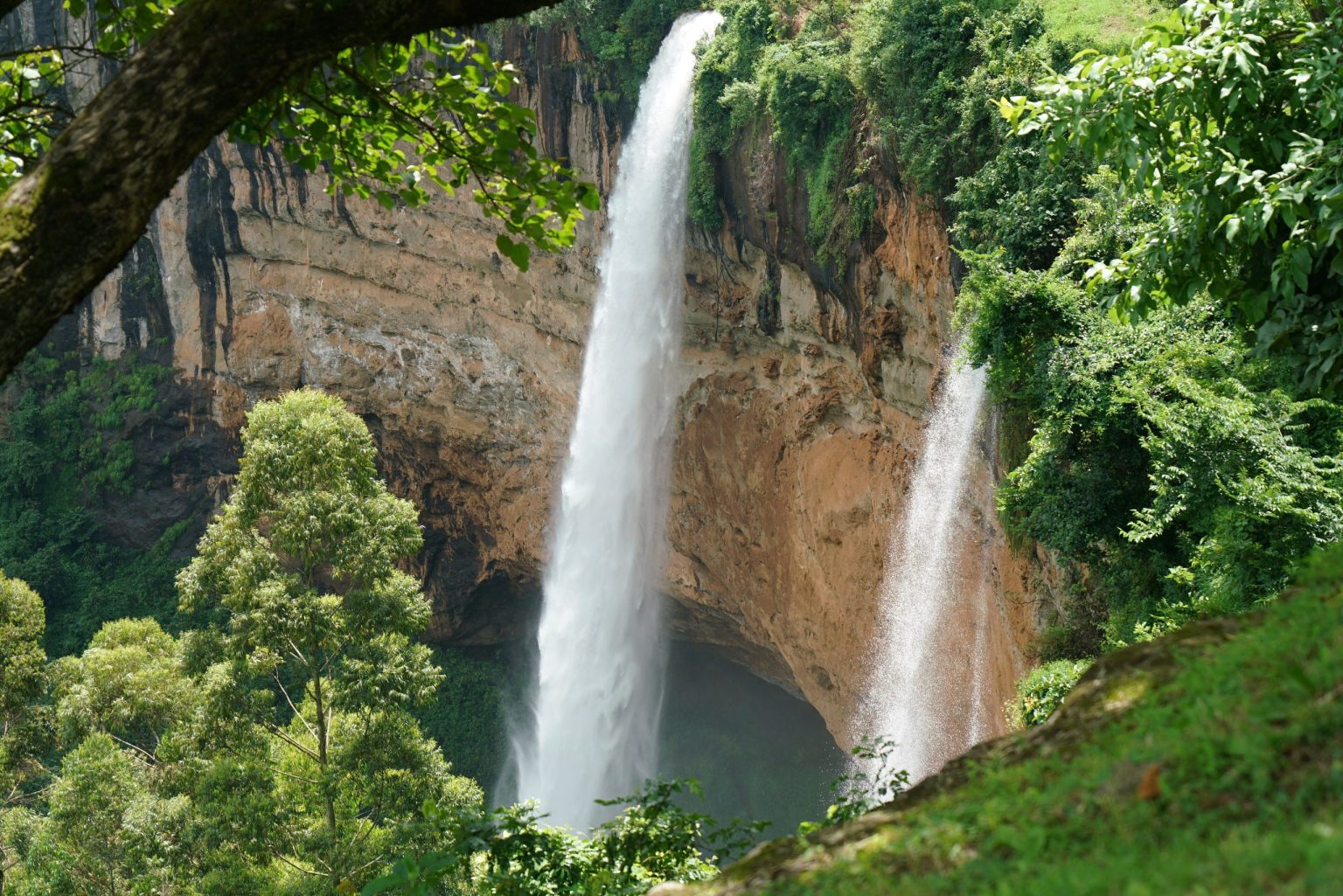 Two waterfalls dropping from a curved cliff into forest at Sipi, eastern Uganda.