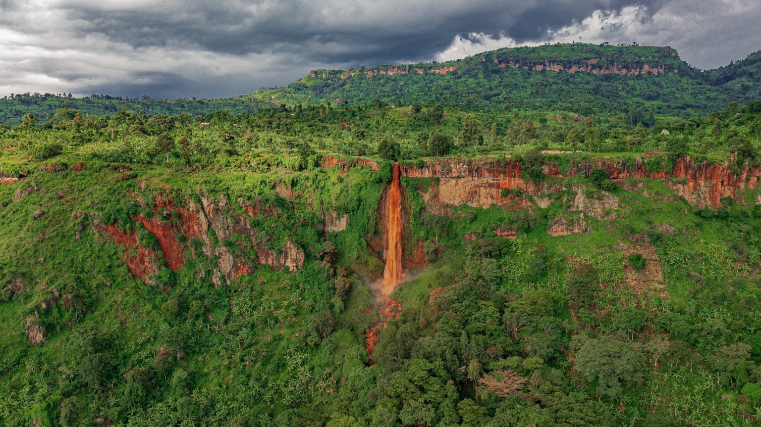 Sisiyi Falls dropping down a red rock cliff into a green valley in Bulambuli.