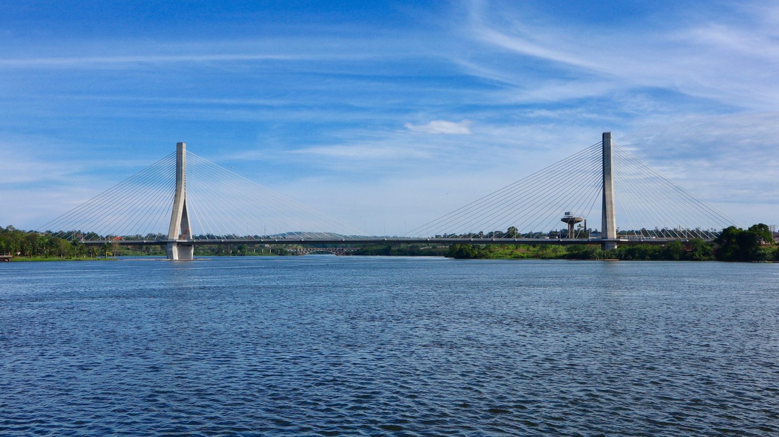The cable-stayed Source of the Nile bridge spanning the river at Jinja under a blue sky.